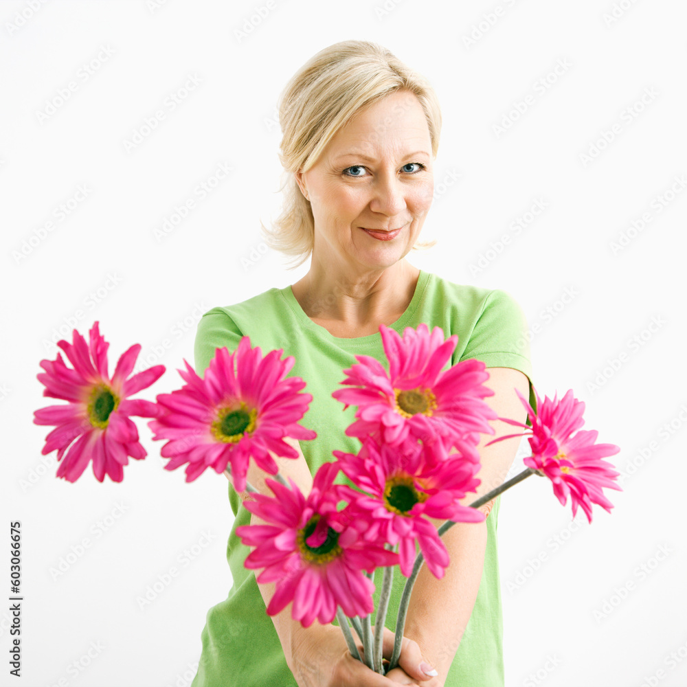 Portrait of smiling adult blonde woman giving bouquet of pink flowers to viewer.