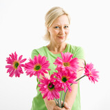 Portrait of smiling adult blonde woman giving bouquet of pink flowers to viewer.
