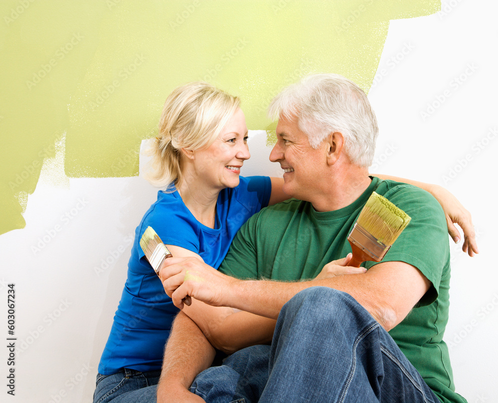 Middle-aged couple snuggling in front of wall they are painting green. Middle-aged couple snuggling in front of wall they are painting green.