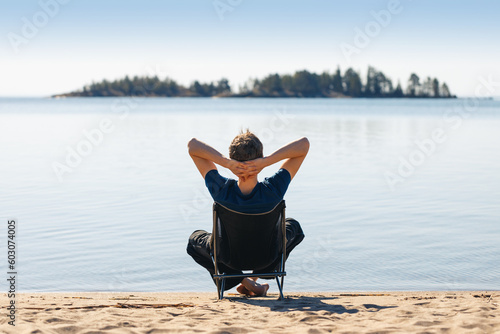 A man is resting in a camping chair on the seashore.