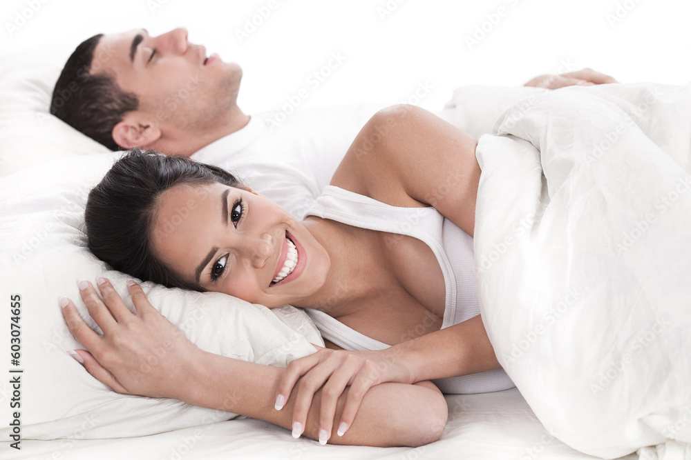 Couple lying in bed together, man sleeping and woman smiling cover in white sheet Couple lying in bed together, man sleeping and woman smiling cover in white sheet