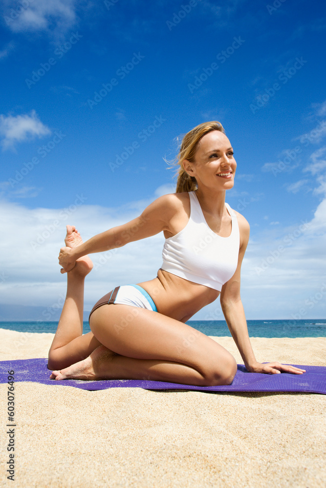 Attractive young woman practices yoga on a sandy beach. The ocean can be seen in the distance. Vertical shot.