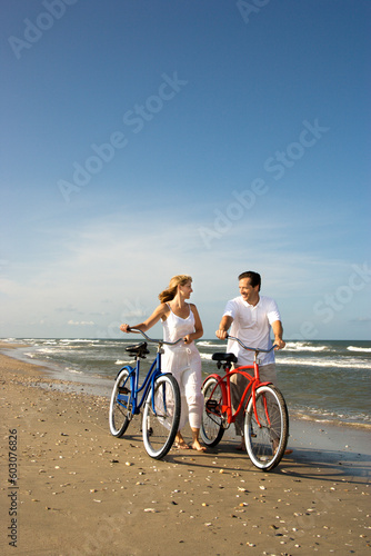 Smiling man and woman walk bicycles down the beach coast. Vertical shot.