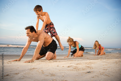 Obraz na plátne Family at the beach playing leap frog. Horizontal shot.