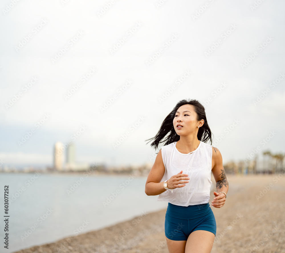 Cheerful east-Asian ethnicity young woman running on the sandy sea beach in summer sports clothing, working out Cheerful east-Asian ethnicity young woman running on the sandy sea beach in summer sports clothing, working out
