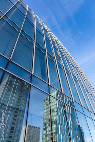 The blue sky is reflected in the windows of a modern office building. Architecture and exterior of contemporary houses