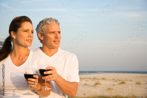 Couple drink red wine at the beach and gaze into the distance together. Horizontal shot. © Designpics