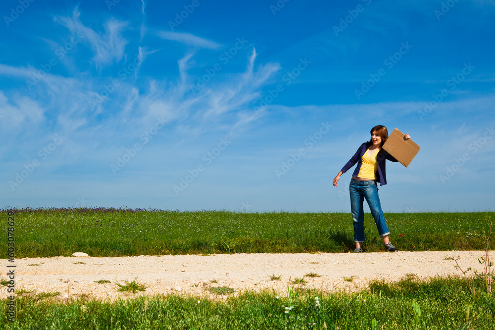 Young woman hitch hiking on a beautiful green meadow