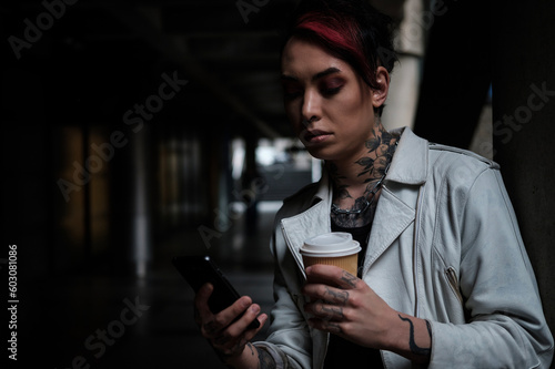 Androgynous male with coffee cup reading on phone.
