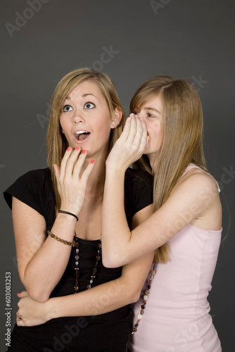 Teenage girls telling secrets posed in front of a gray background