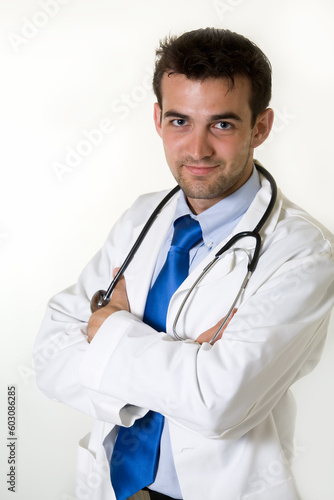 Young attractive man doctor wearing white lab coat and blue tie with a stethoscope around shoulders with arms crossed © Designpics