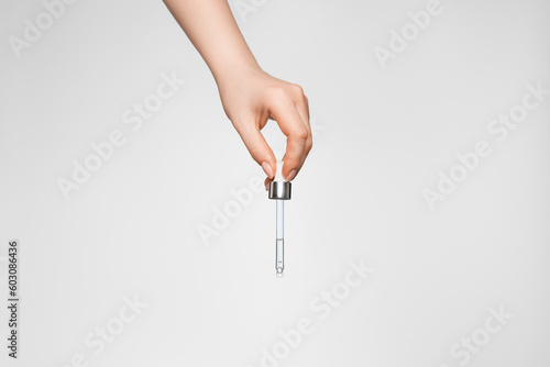 Female hand on a light background with a pipette.