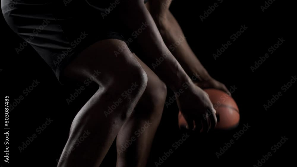 Basketball player bouncing a ball. African american sports man practicing against black background. Abstract body shot side view. Basketball player bouncing a ball. African american sports man practicing against black background. Abstract body shot side view.