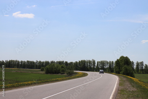 White car on an asphalt road near the village of Konstantinovo on a sunny spring day
