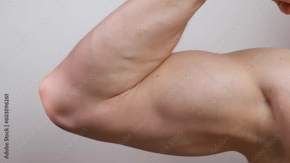The muscular arm of the athlete squeezes and shows the biceps in close-up on a white background. The concept of health and physical strength The muscular arm of the athlete squeezes and shows the biceps in close-up on a white background. The concept of health and physical strength