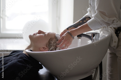 Crop hairstylist washing hair of client in salon photo