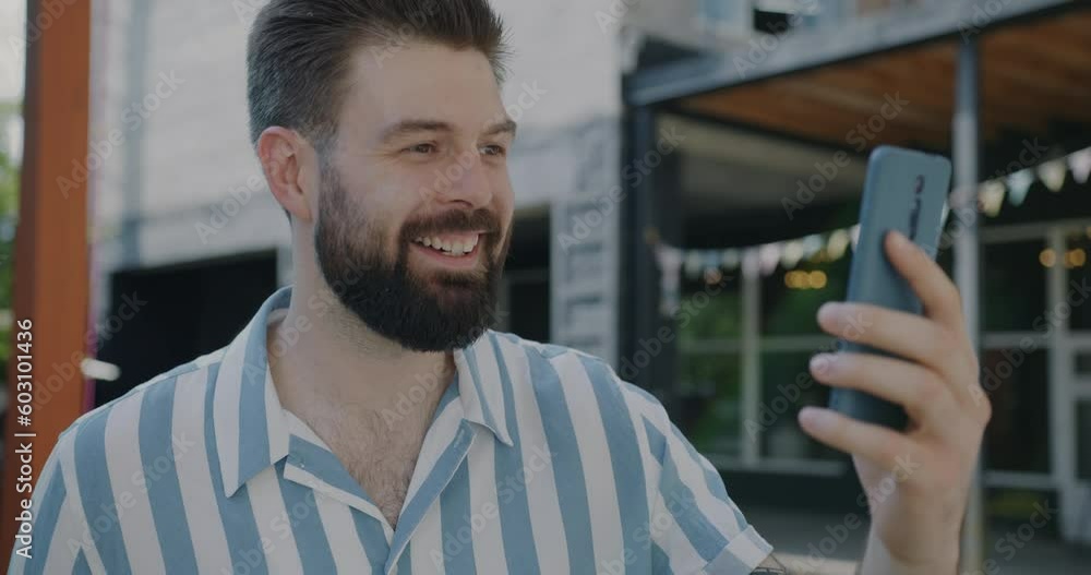 Joyful guy chatting on smartphone making online video call talking and laughing outdoors in city. Young people and communication concept. Joyful guy chatting on smartphone making online video call talking and laughing outdoors in city. Young people and communication concept.