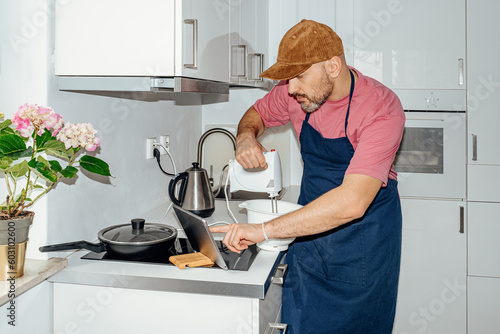 A focused man whips with a mixer in the kitchen photo
