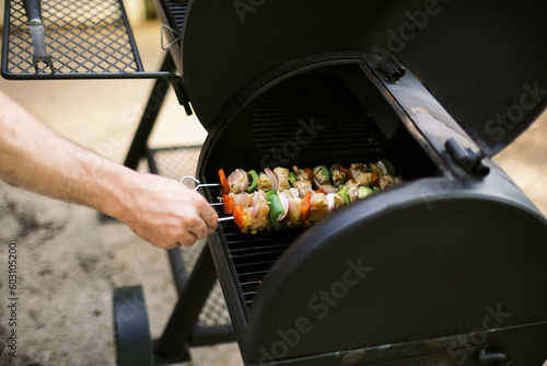 man grilling chicken shish kebab skewers on the bbq grill photo
