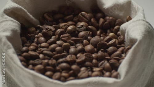 Shot slightly from above, medium shot of falling coffee beans into a rag bag. Rag bag in white. Hot roasted black coffee.