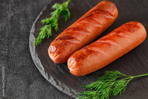 Grilled sausages with cuts, on slate stone plate round, dark background, selective focus 