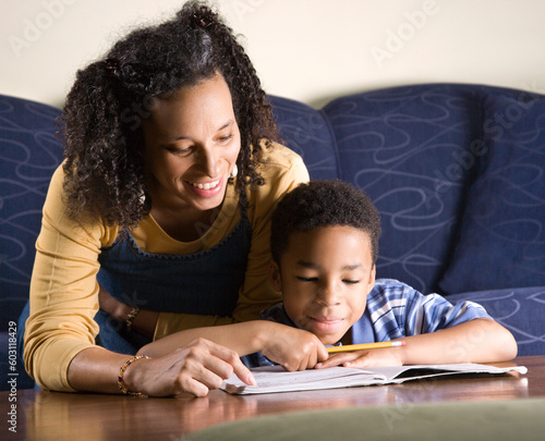 A mid adult African American woman sits on a couch while helping her young some with his homework. Horizontal shot.