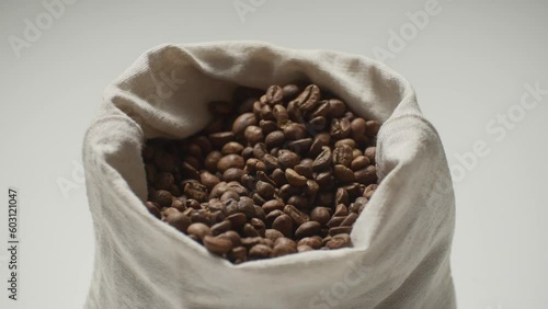 Medium shot of a bag of coffee and women's hands, a woman takes a handful of roasted coffee beans and lifts them above the fabric bag