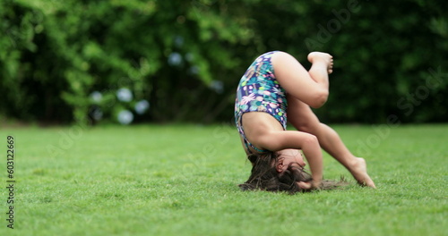 Happy child girl rolling on lawn outdoors, tumbling down, kid doing somersault