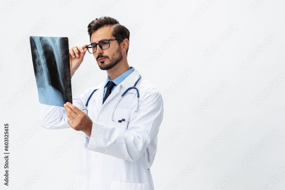 Male doctor in white coat and eyeglasses and stethoscope looks thoughtfully at pictures of X-ray patient for diagnosis on white isolated background, copy space, space for text, health - obrazy, fototapety, plakaty 