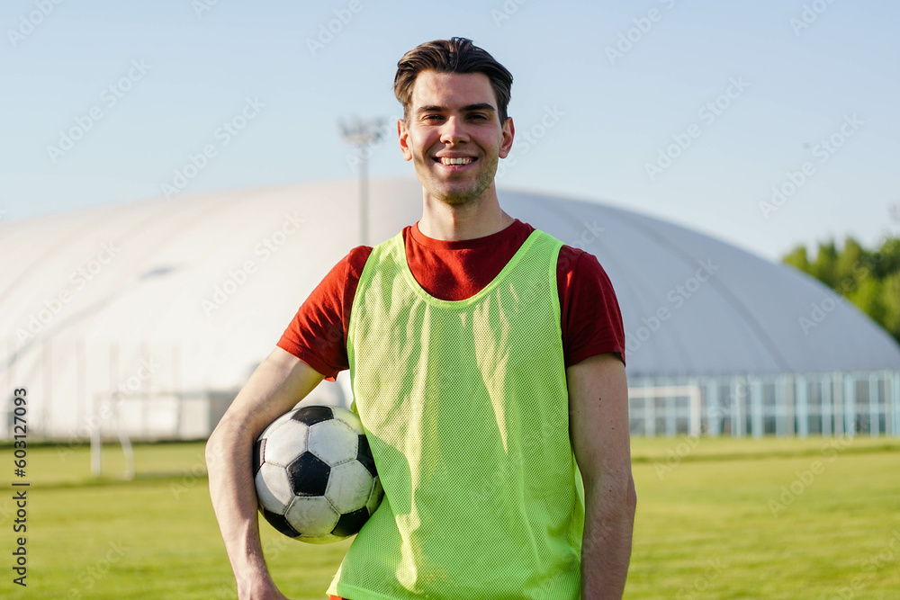 Portrait of a smiling young man football player with a soccer ball at sunset