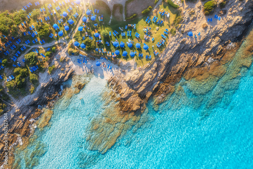 Aerial view of sea bay, sandy beach with umbrellas, stones and rocks in water at sunset in summer. Sardinia, Italy. Tropical scenery with sea lagoon, swimming people, blue water. Drone view from above