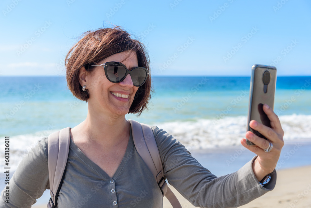 Smiling woman taking a selfie on a sandy beach in California on a sunny autumn day