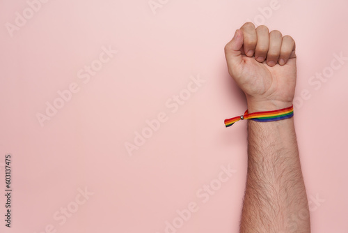 Proudly raised fist with rainbow-colored bracelet on a pink background