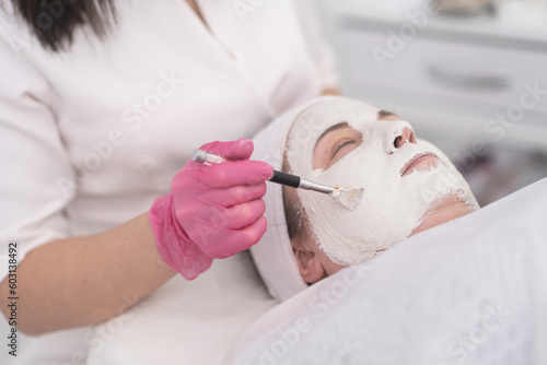 close up Cosmetician hands in pink gloves applying a facial beauty mask using a brush.