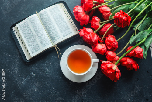Open bible with tulip flowers and a cup of tea on a dark background #603141017