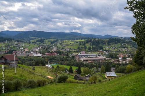 Picturesque scenery of rolling countryside with rural houses of a Carpathian mountain village on green hills under cloudy sky. Vorokhta, Ukraine © Dmytro