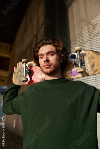 Young trendy male skater stainding in hangar in sunlight photo