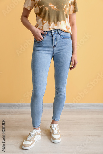 Young woman in stylish jeans near yellow wall