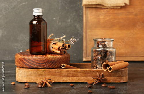 Wooden board with bottle of cosmetic product, cinnamon sticks and anise stars on dark background
