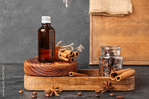 Wooden board with bottle of cosmetic product, cinnamon sticks and anise stars on dark background