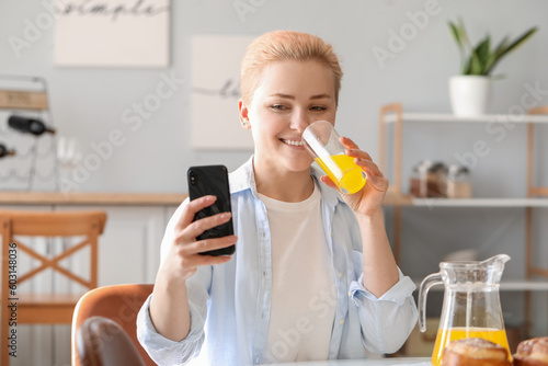 Принти на полотні Young woman with mobile phone drinking juice in kitchen