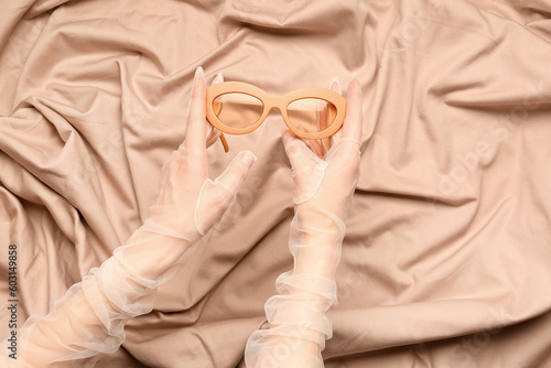 Woman with stylish sunglasses on beige fabric background