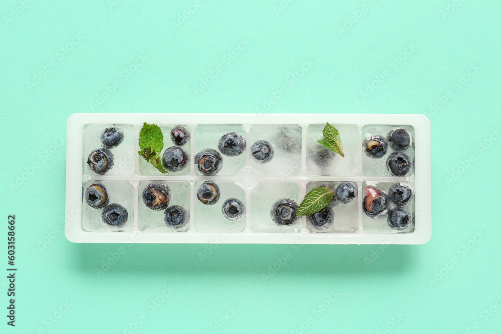 Ice tray with fresh blueberry frozen in ice on blue background Ice tray with fresh blueberry frozen in ice on blue background