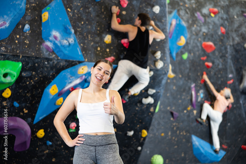 after successful workout, young female sportswoman poses near rock black bouldering wall indoors