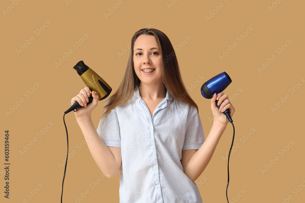 Beautiful young woman with hair dryers on beige background Beautiful young woman with hair dryers on beige background