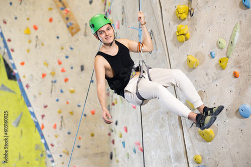 Middle-aged man in safety helmet and with safety rope hangs near climbing wall in gym. active hobby concept