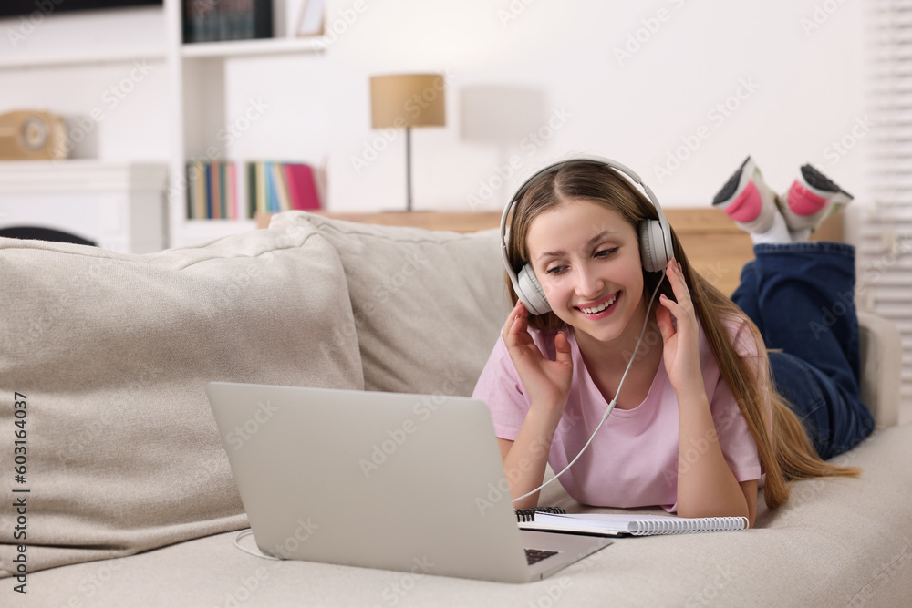 Online learning. Smiling teenage girl in headphones near laptop on sofa at home Online learning. Smiling teenage girl in headphones near laptop on sofa at home
