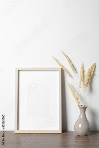 Empty photo frame and vase with dry decorative spikes on wooden table. Mockup for design