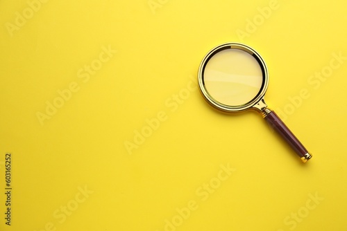 Magnifying glass on yellow background, top view. Space for text