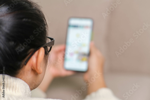 Happy young woman using mobile phone while sitting on sofa at home. Attractive woman holding smartphone checking social media, playing games, online shopping relaxing on sofa.